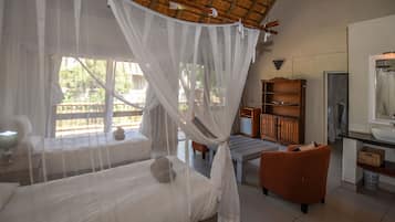 A room with a bed, a daybed, a wooden cabinet, and a window with a view of greenery.