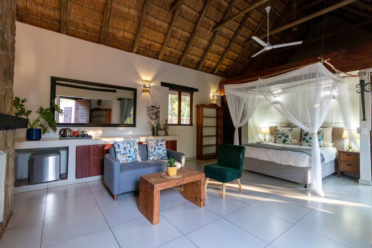 A room with a bed, a sofa, a coffee table, a chair, a ceiling fan, and a large window.