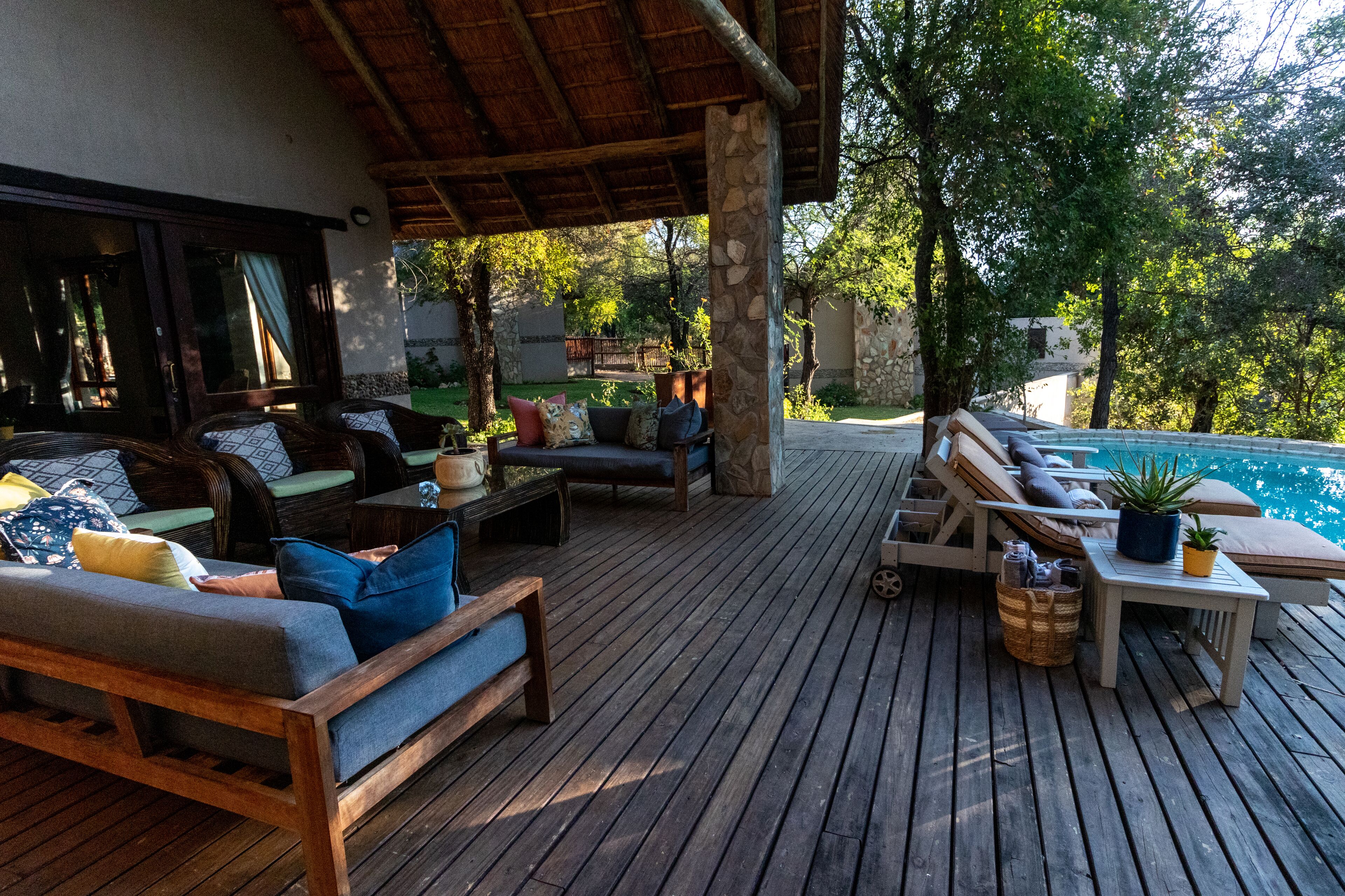 A wooden deck with outdoor seating, a pool, and a stone wall.