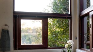 A large, oval-shaped hot tub with a stone exterior, positioned next to a window with a view of greenery outside. - Leopard's Lair Bush Lodge (Hoedspruit)