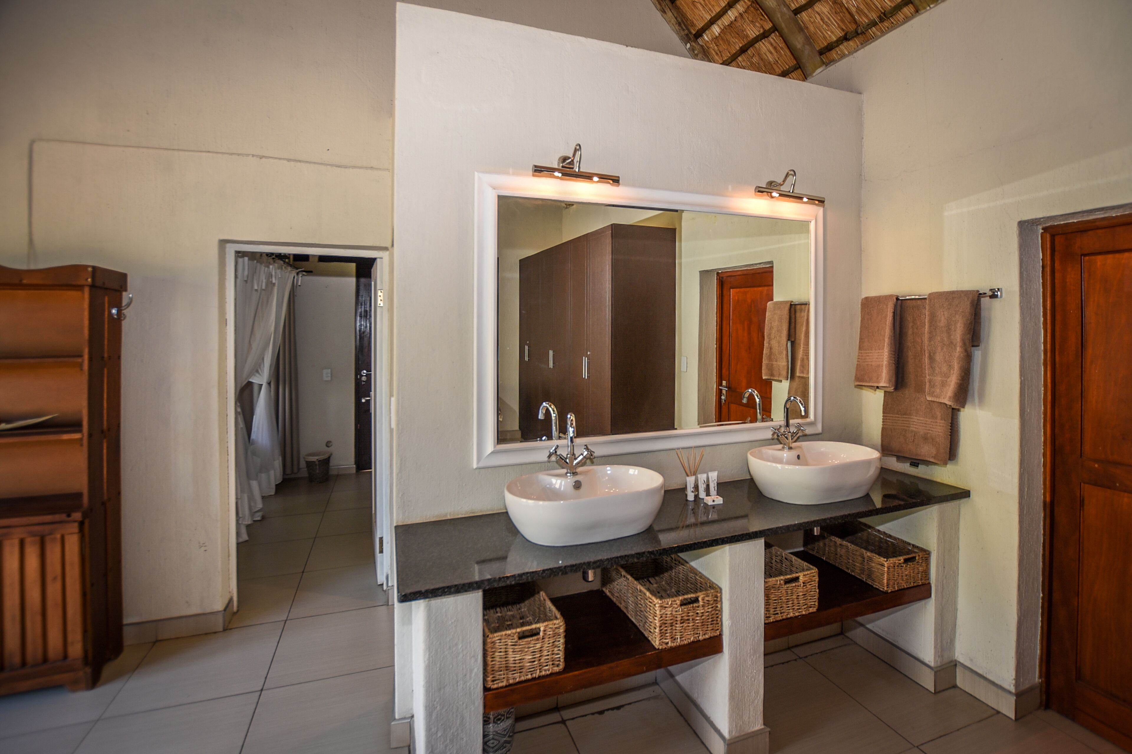 A bathroom with two sinks, a large mirror, and wicker baskets on the countertop.