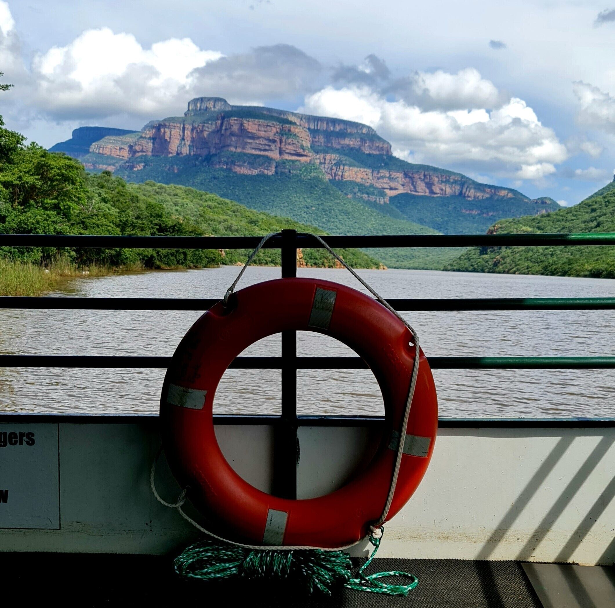 A lifebuoy hanging on a railing with a view of a mountainous landscape in the background.