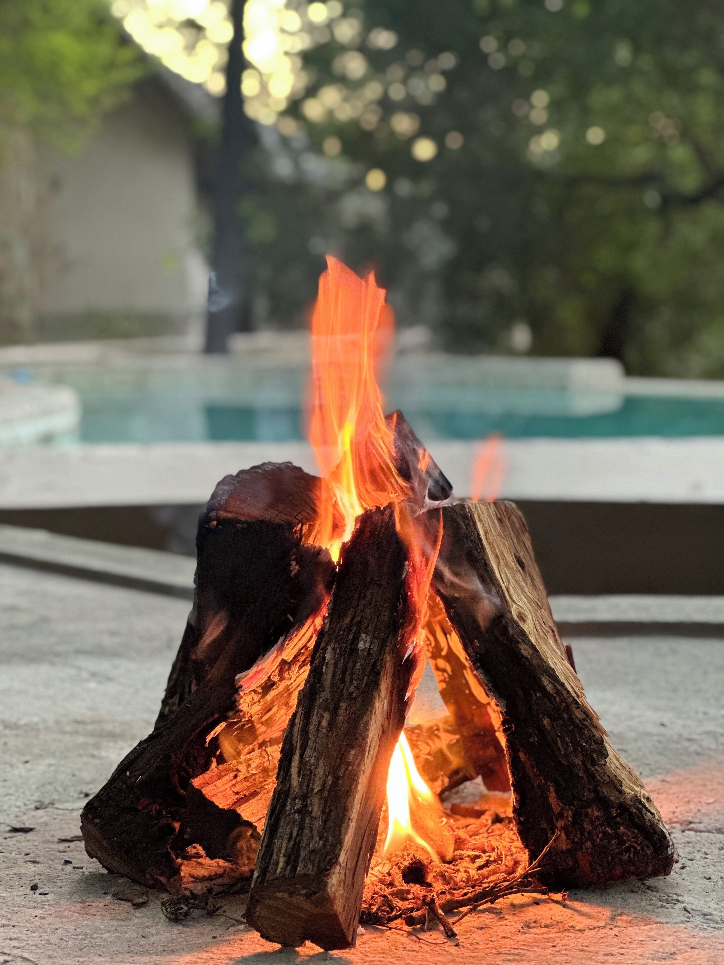 Fuego ardiendo en un área de concreto con una piscina al fondo.
