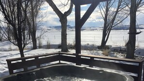 Un jacuzzi bajo una pérgola de madera, con un paisaje nevado y árboles al fondo.