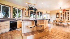 Una cocina amplia con armarios de madera, una isla central con taburetes y una zona de comedor con sillas de madera.