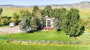 Una casa grande con un porche delantero destacado, rodeada de árboles altos y un patio cercado.