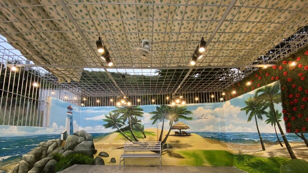 Un espacio interior con un mural de playa, una cabaña de techo de paja y un banco.