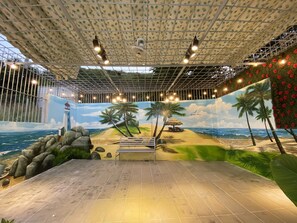 Un espacio interior con un mural de playa, una cabaña de techo de paja y un banco.