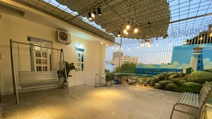 Amplio espacio interior con techo alto, un mural de una escena costera y una zona de estar con bancos y plantas en macetas.