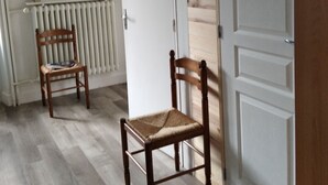 Una habitación con dos sillas de madera, un radiador, una puerta blanca y un cuadro con una imagen de ciervo en la pared.