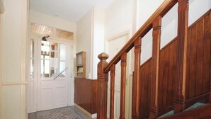 Un pasillo con una escalera de madera, piso estampado y una puerta blanca que da a una habitación.