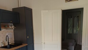 Un espacio habitable compacto con kitchenette, piso estampado, sofá con cojines, una puerta que conduce a un dormitorio y una lámpara colgante.