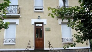 Un edificio con una puerta central de madera, escalones de piedra y barandillas de metal.