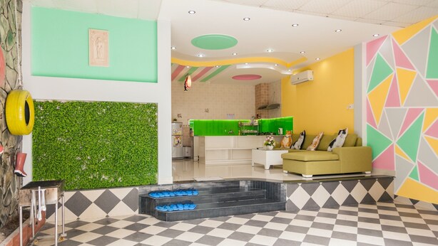 Een hal met een zwart-wit geruit vloerkleed, een groene muur met een muurschildering, een receptiebalie en een bank met kussens.