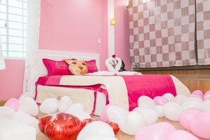 Une chambre à coucher décorée dans des tons de rose, avec un lit, des oreillers et un animal en peluche décoratif.