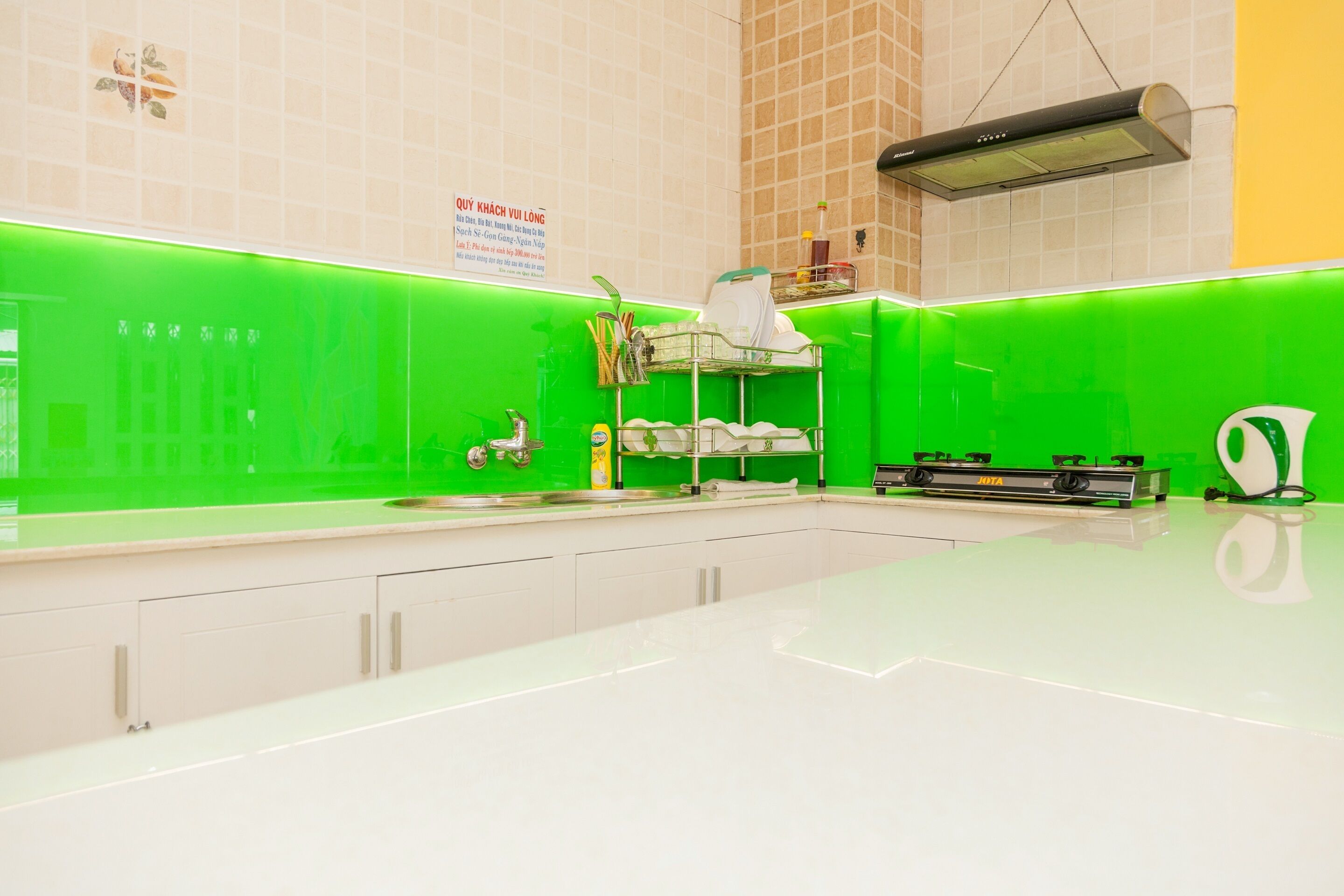 A modern kitchen with a green backsplash, white countertops, and a stainless steel range hood.