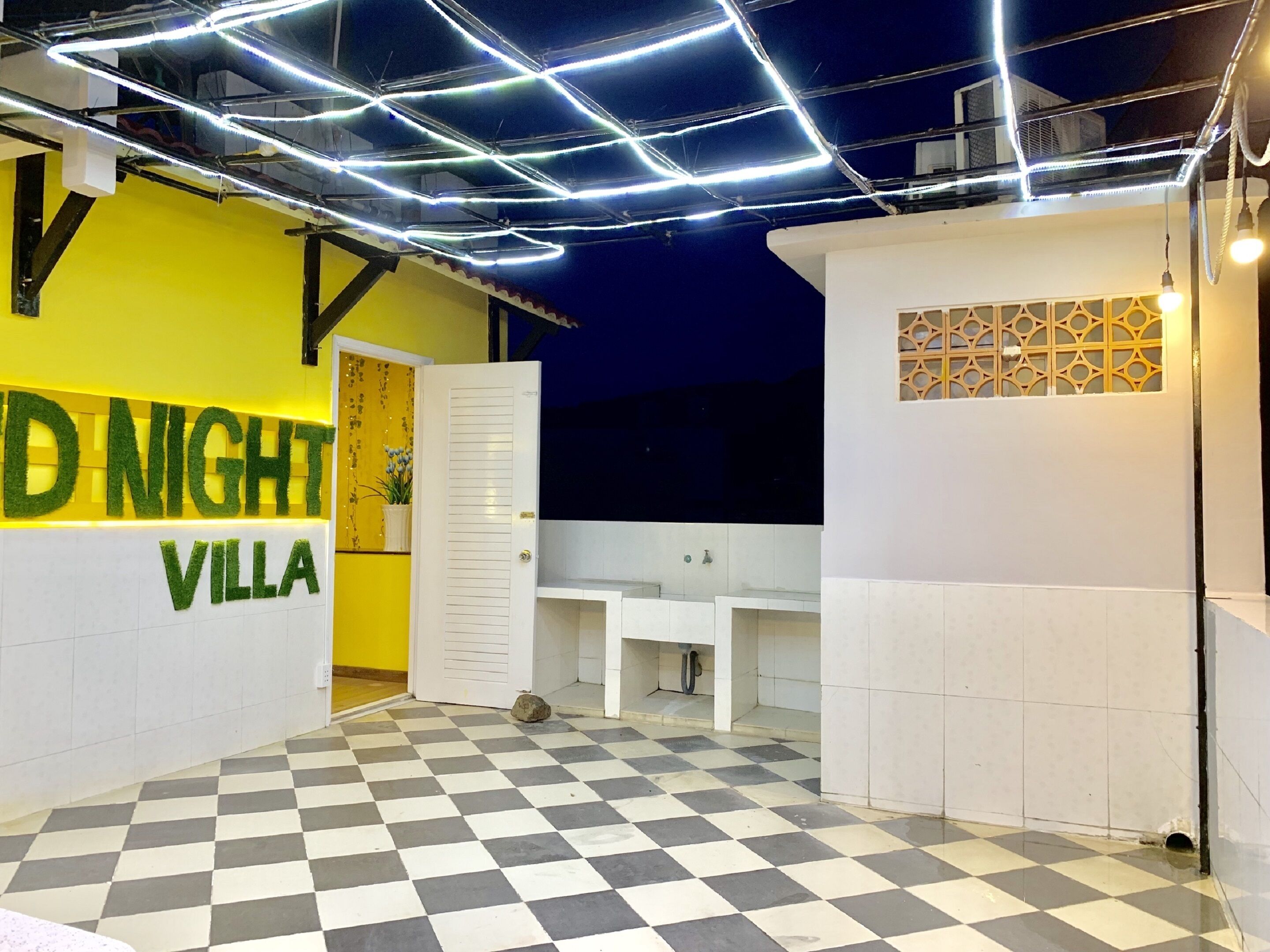 Interior de un hotel con piso a cuadros, un mostrador de recepción blanco y una pared amarilla con el texto 