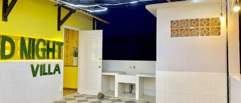 Interior de un hotel con piso a cuadros, un mostrador de recepción blanco y una pared amarilla con el texto
