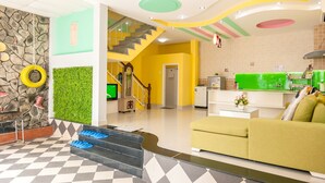 Een hotelhal met een zwart-wit geruit vloerkleed, een trap, een receptiebalie en een groene muur met een klok.