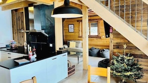 Una cuina moderna amb una illa central, una zona de menjador amb taula de fusta i una escala que condueix a un nivell superior.