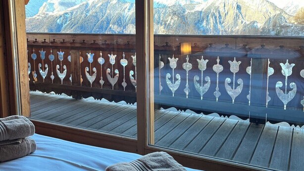 Una habitació amb un llit, una barana de fusta i vistes a muntanyes nevades.