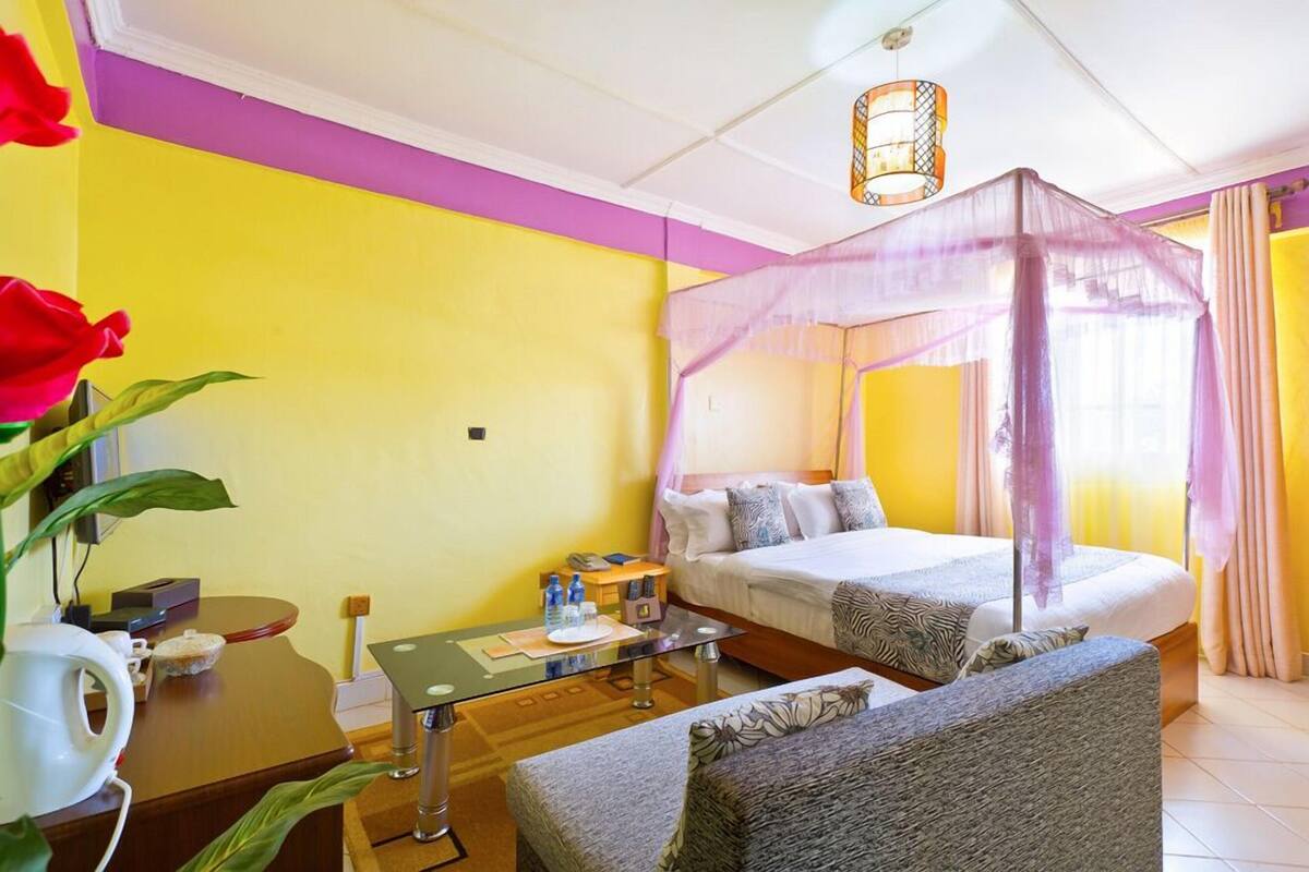 Una habitación de hotel con una cama, un diván, una mesa con un florero y una mesita de noche con una lámpara.