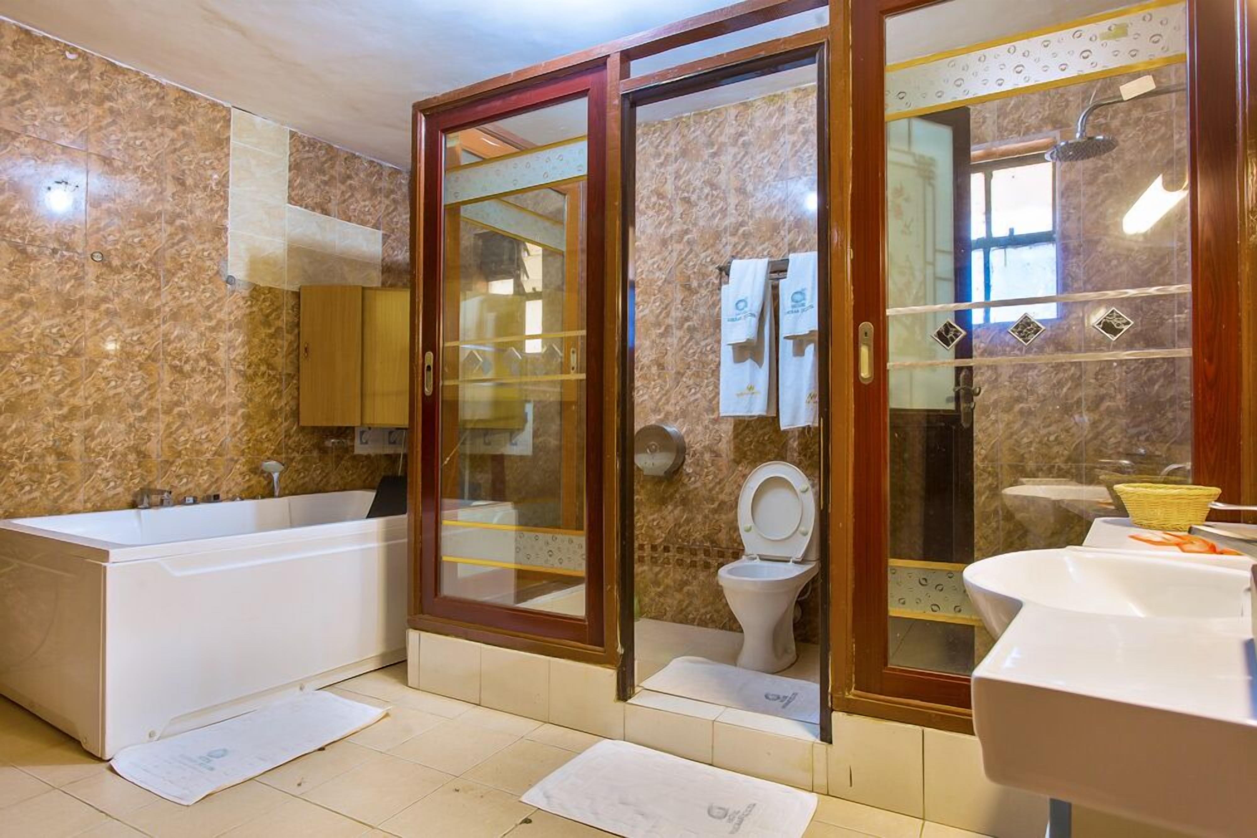 A bathroom with a bathtub, toilet, and sink, featuring marble walls and wooden-framed glass doors.