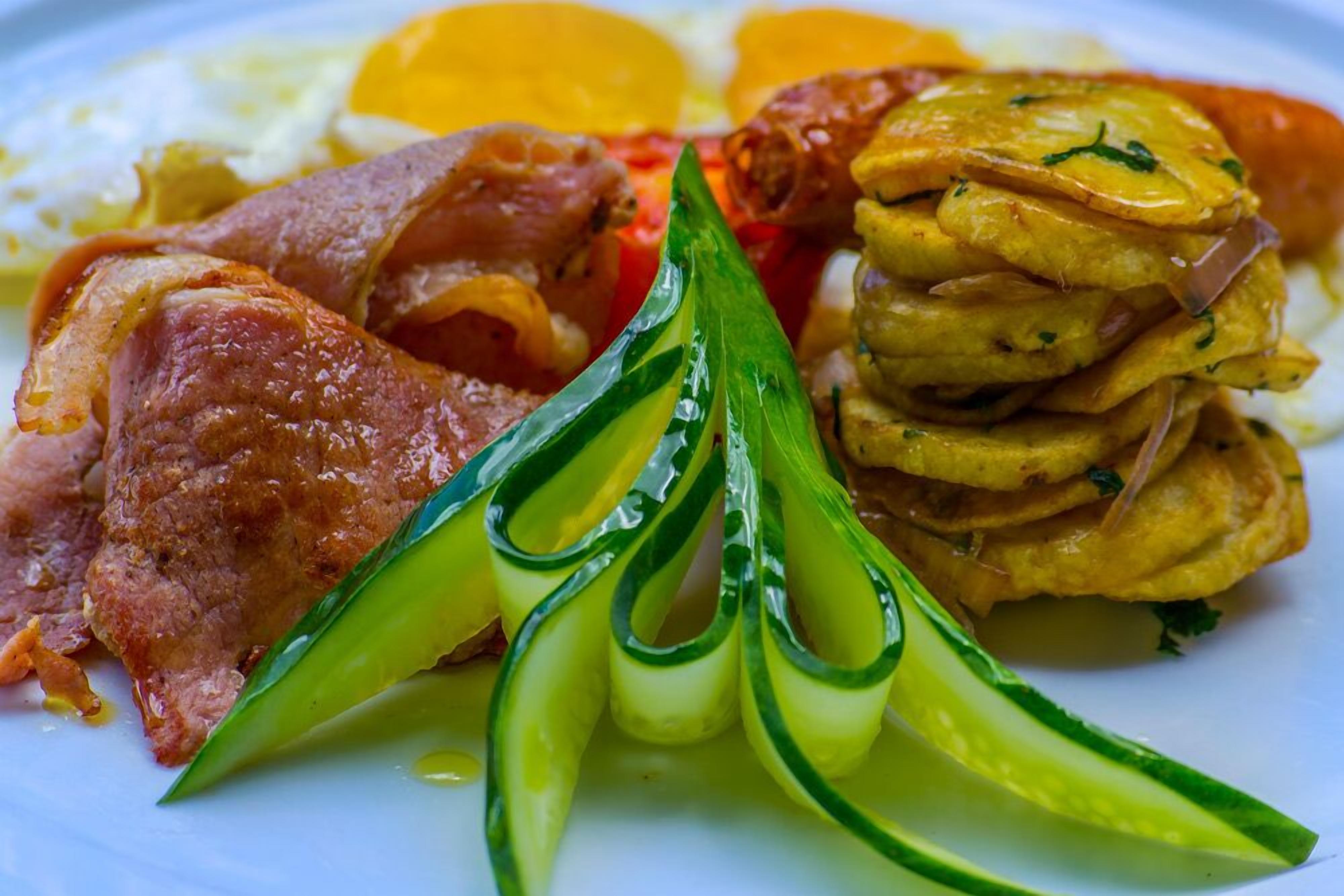 Un plato con diversos alimentos para el desayuno, como tocino, huevos y pepino en rodajas.