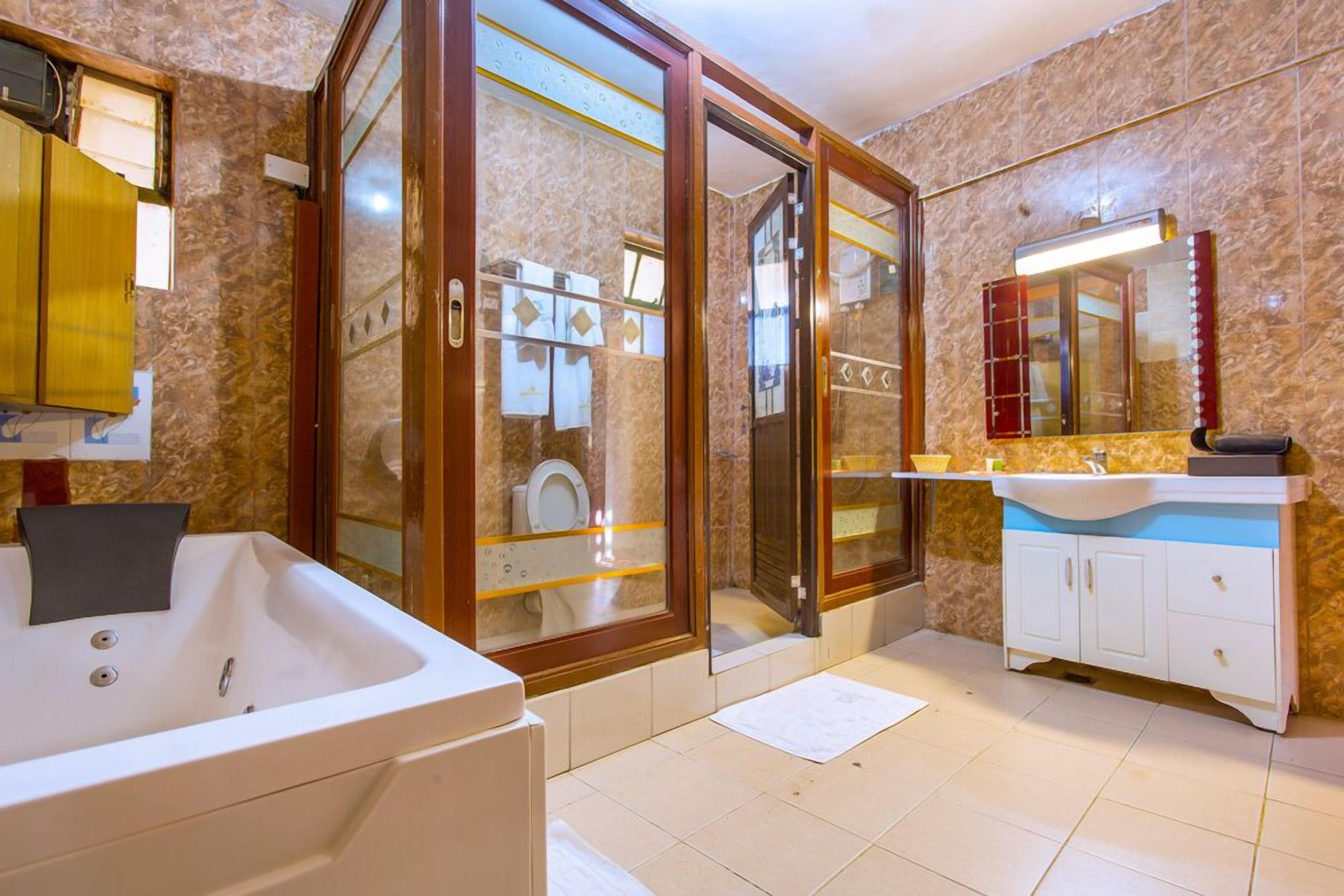 Une salle de bain dotée d’une grande baignoire, d’une douche à parois de verre, d’un meuble-lavabo avec un miroir et de toilettes visibles à travers la porte de la douche.