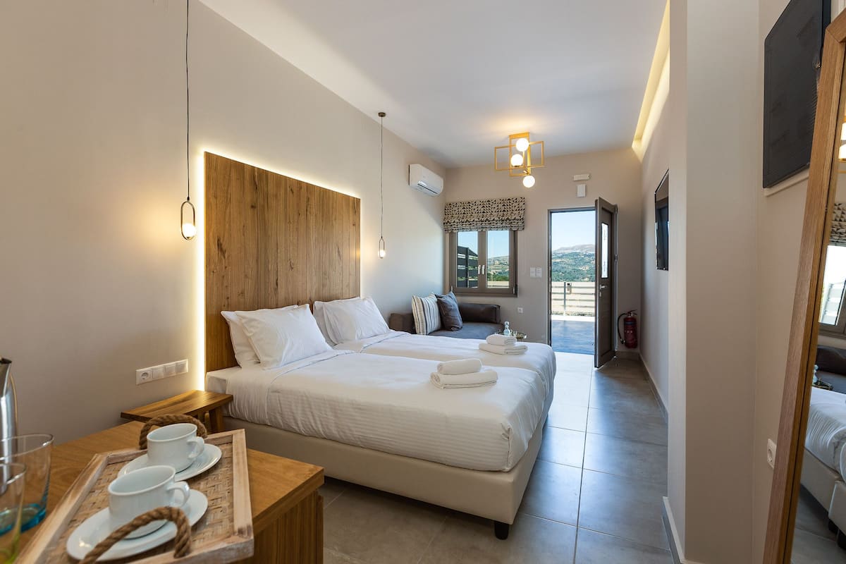 A modern hotel room with a large bed, bedside tables, a wooden headboard, and a view of the outdoors.
