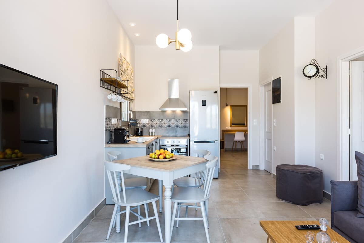 A modern kitchen with white cabinetry, a dining table with chairs, a refrigerator, and a hanging light fixture.