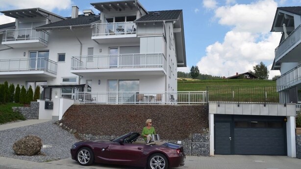A modern multi-story residential building with balconies, a driveway, and a parked car. - FeWo Sonne (Oberstaufen)