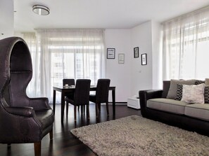 A modern living room with a dining area, featuring a leather armchair, a sofa, and a fluffy rug.