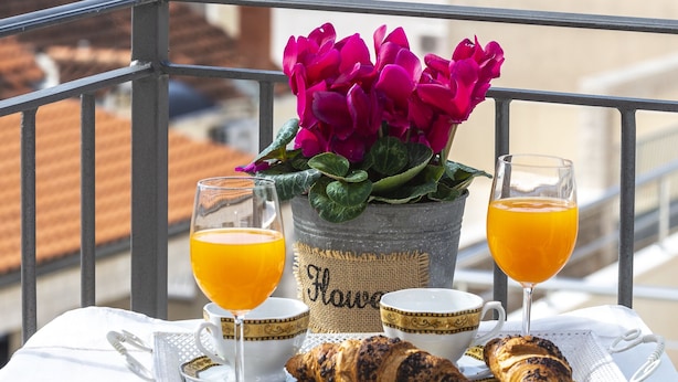 A balcony table with croissants, a glass of orange juice, a glass of orange juice, a cup, and a potted plant with pink flowers. - Villa Boro 2 (Dubrovnik)