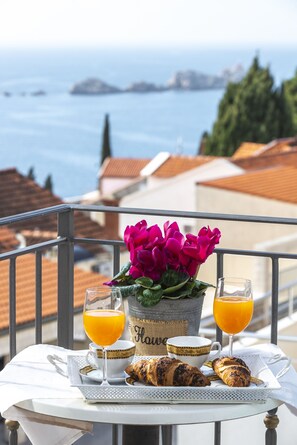 A balcony table with croissants, a glass of orange juice, a glass of orange juice, a cup, and a potted plant with pink flowers. - Villa Boro 2 (Dubrovnik)