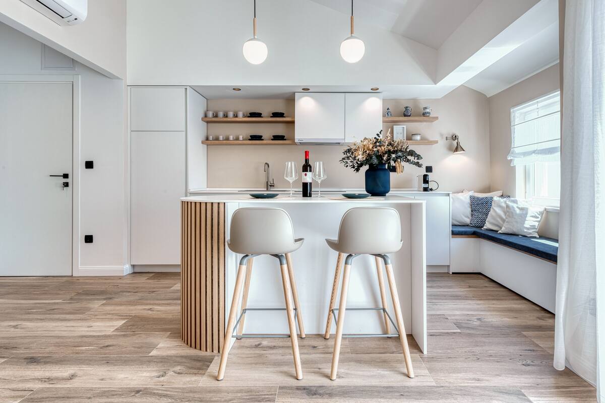Une cuisine moderne avec des meubles blancs, un îlot central doté de tabourets et un coin salon offrant une vue agréable.