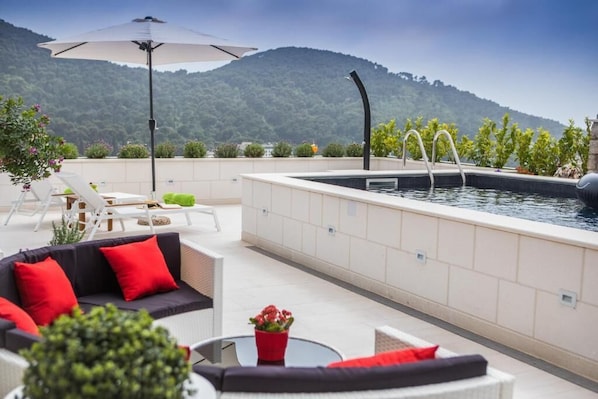 A rooftop pool area with a view of a mountain, outdoor seating, and a water feature.