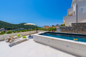 A rooftop pool area with lounge chairs and a view of the city and hills.