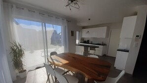 A modern kitchen with white cabinets, a wooden dining table, and a water dispenser. - Beautiful new contemporary house 2 min walk from the beaches of Cabellou (Concarneau)