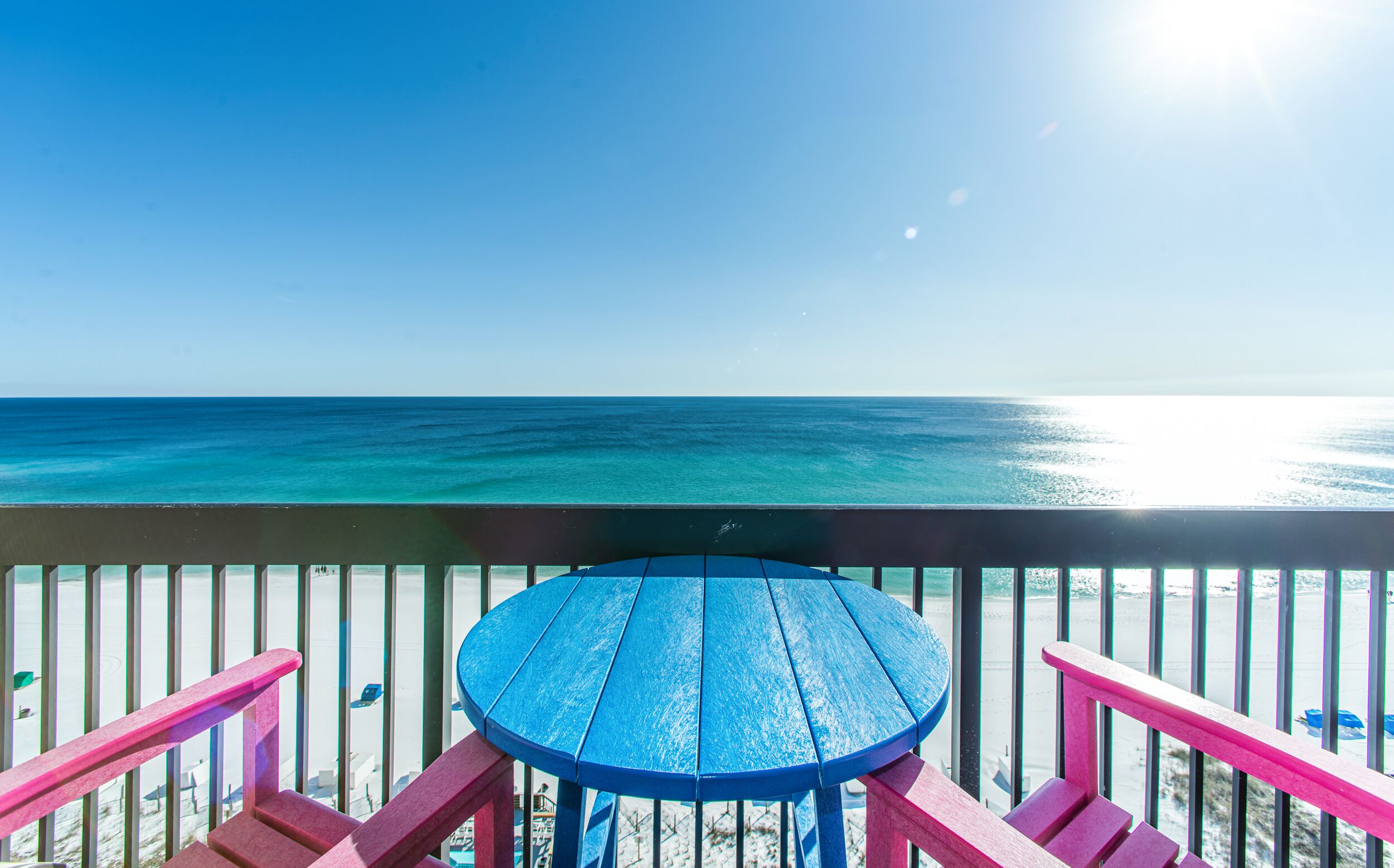 A blue table and pink railings on a balcony overlooking the ocean.