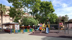 Un terrain de jeux doté de diverses installations, notamment des toboggans et des structures d’escalade, entouré d’arbres et avec un bâtiment visible au loin.