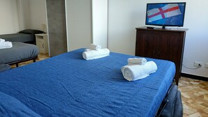 Une chambre d’hôtel avec un grand lit, un téléviseur posé sur une commode en bois et un bureau avec une lampe.