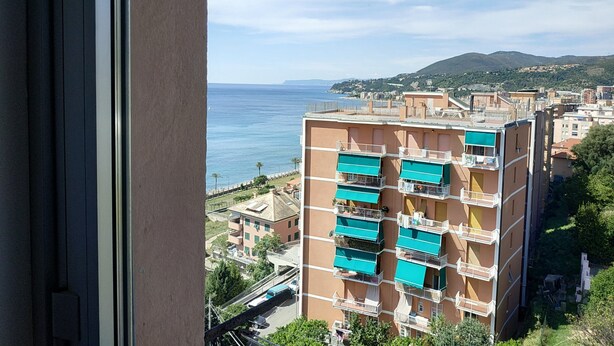 Un immeuble à plusieurs étages doté de balcons, offrant une vue sur la mer et s’inscrivant dans un paysage vallonné en arrière-plan.