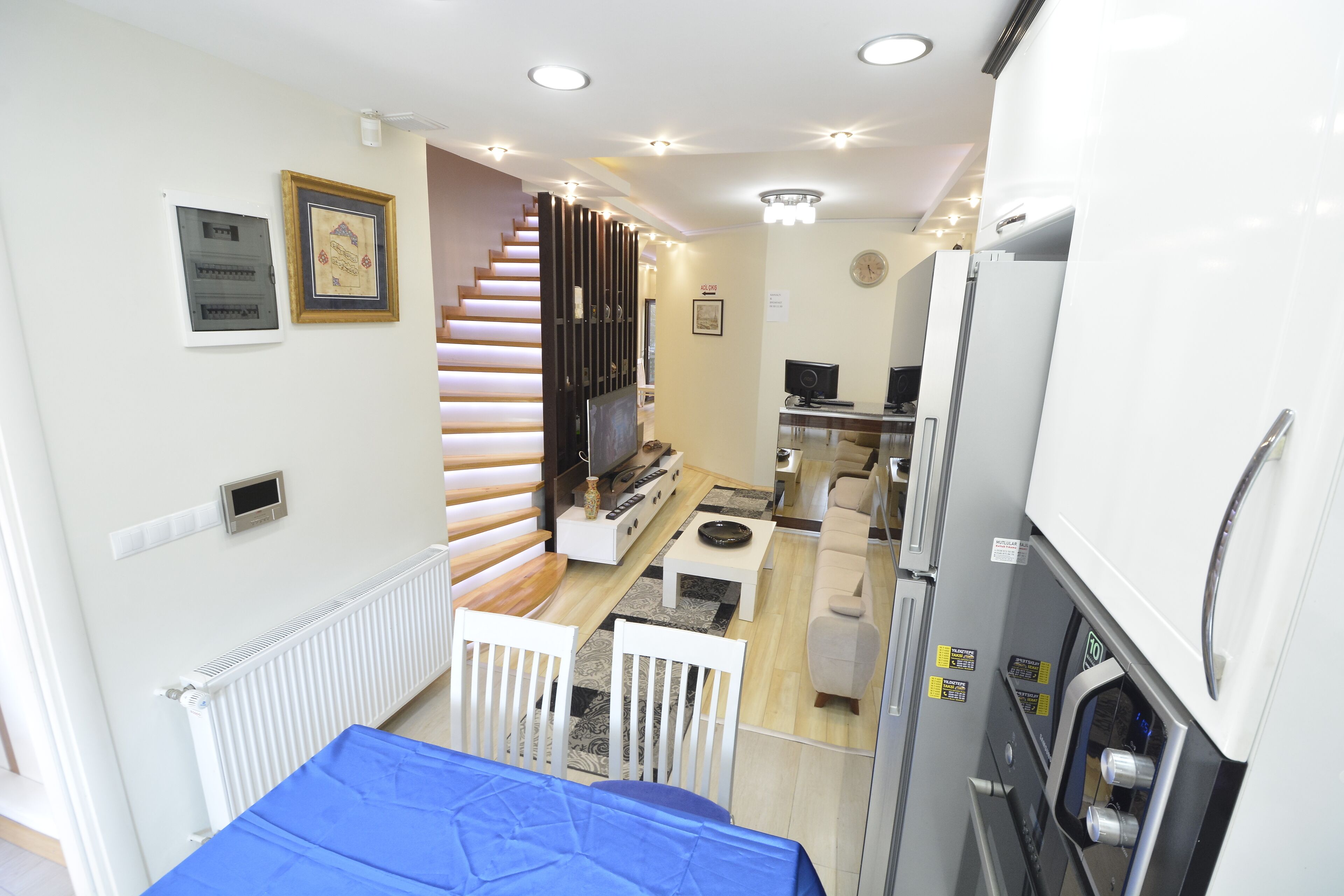 Quarto de hotel compacto com cama, cozinha compacta, pequena área de refeições e escada para outro nível.