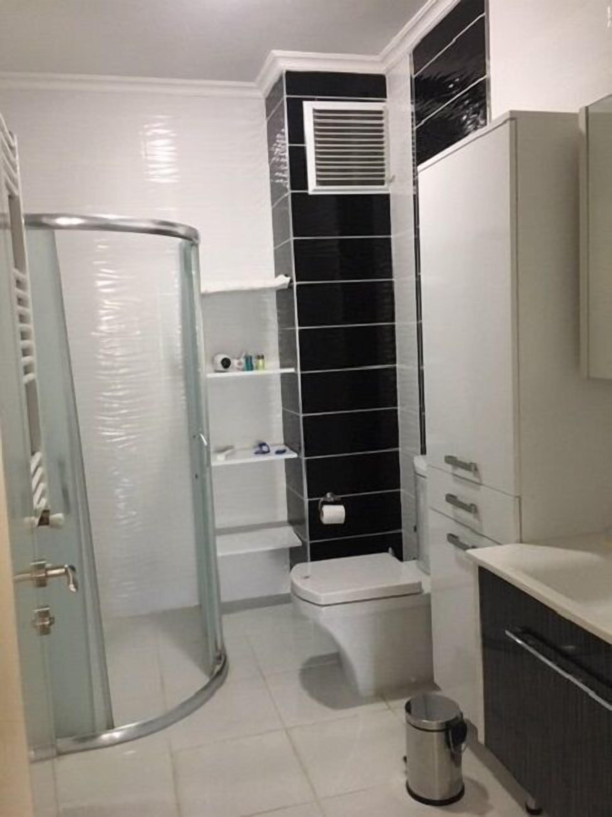 Et badeværelse med en glasvægshafsprængning, toilet, vask og skraldespand.