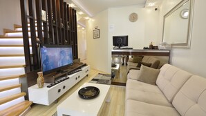 A modern living room with a flat-screen TV, a sofa, a coffee table, and a staircase with wooden railings. - Mavi Deniz Butik Otel (Mudanya)