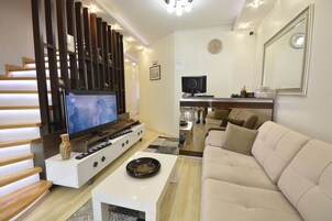 Una sala de estar moderna con una televisión de pantalla plana, un sofá, una mesa de centro y una escalera con barandilla de madera.