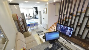 A modern living room with a large flat-screen TV, a computer, and a coffee table. There is a sofa and a dining area in the background. - Mavi Deniz Butik Otel (Mudanya)