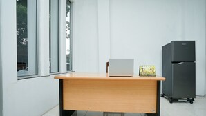 A wooden desk with a laptop and a small box, a black refrigerator, and a window with a view of trees. - Hotel O Choco 88 Residence (Dringu)