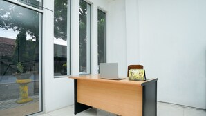 A modern office desk with a laptop and a decorative lamp, positioned near large windows with a view of trees and a yellow fire hydrant outside. - Hotel O Choco 88 Residence (Dringu)